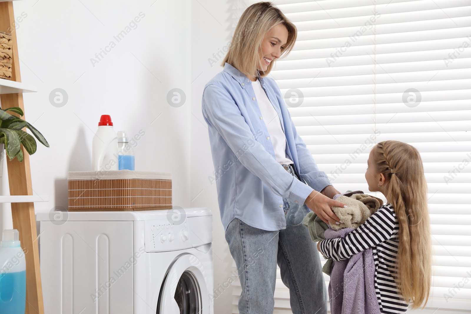 Photo of Little girl helping her mom doing laundry at home