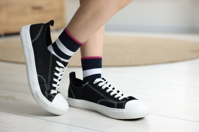 Photo of Child wearing stylish oversized sneakers indoors, closeup