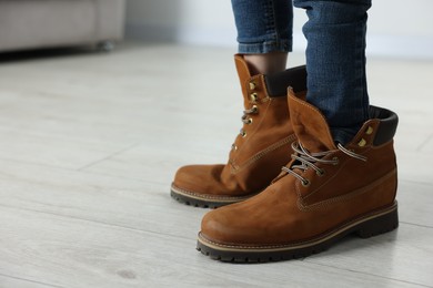 Child wearing oversized brown boots indoors, closeup. Space for text