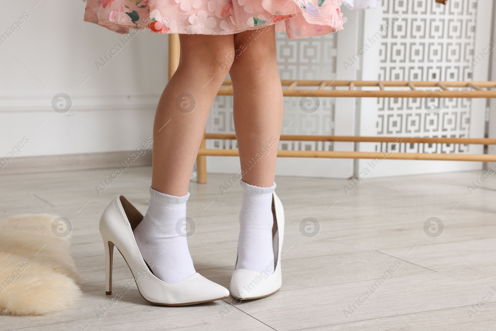 Photo of Little girl wearing oversized high heeled shoes indoors, closeup. Space for text