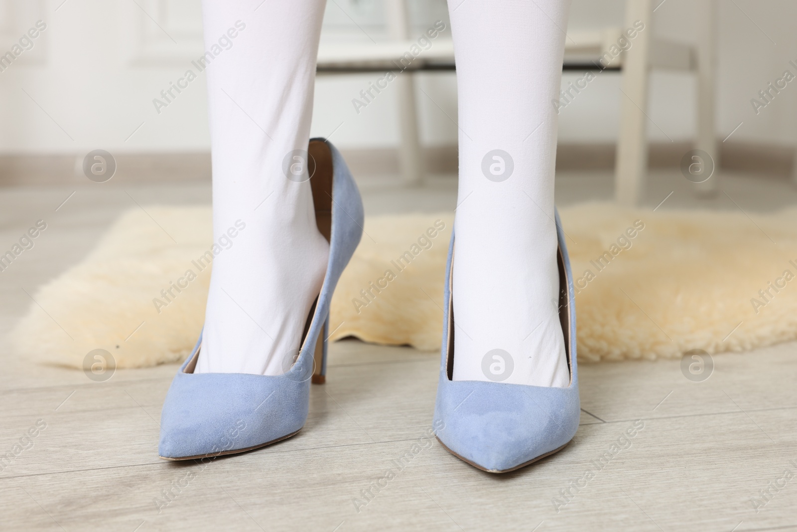 Photo of Little girl wearing oversized high heeled shoes indoors, closeup