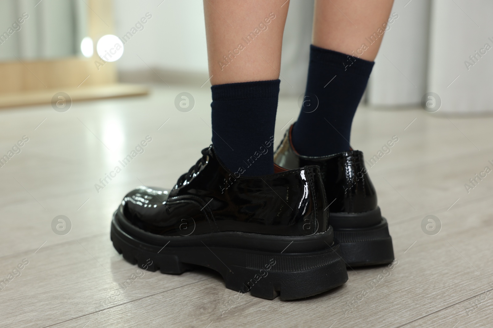 Photo of Little girl wearing oversized shoes indoors, closeup