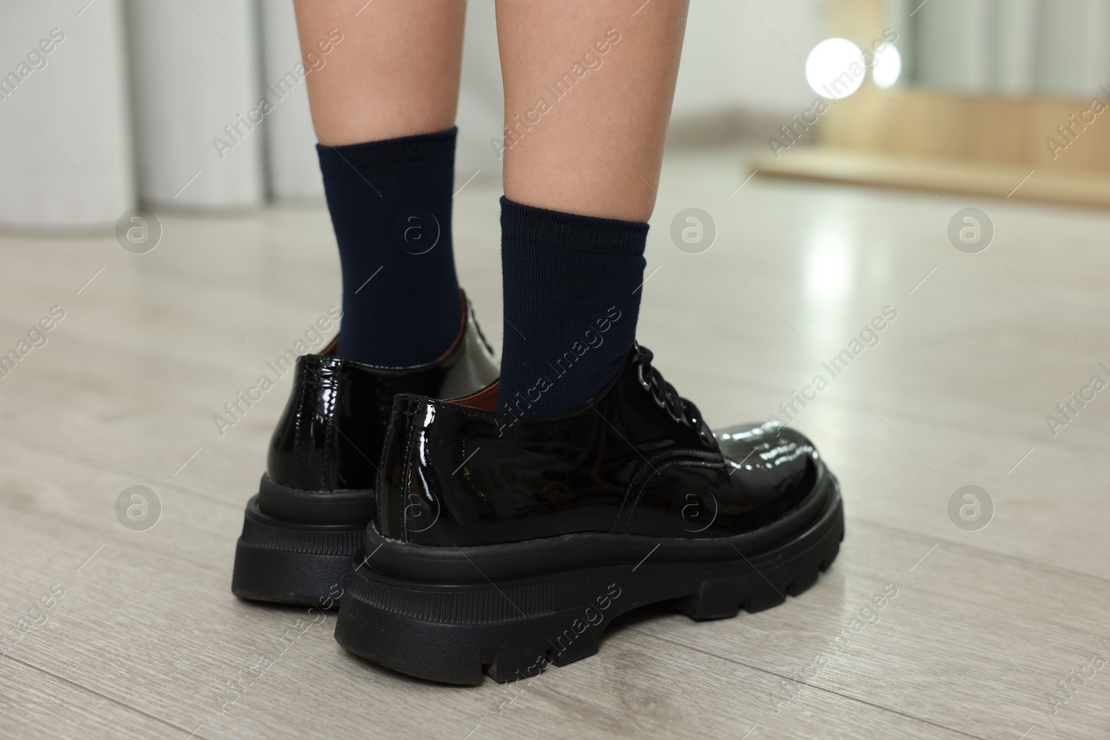 Photo of Little girl wearing oversized shoes indoors, closeup