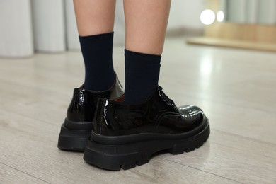 Photo of Little girl wearing oversized shoes indoors, closeup