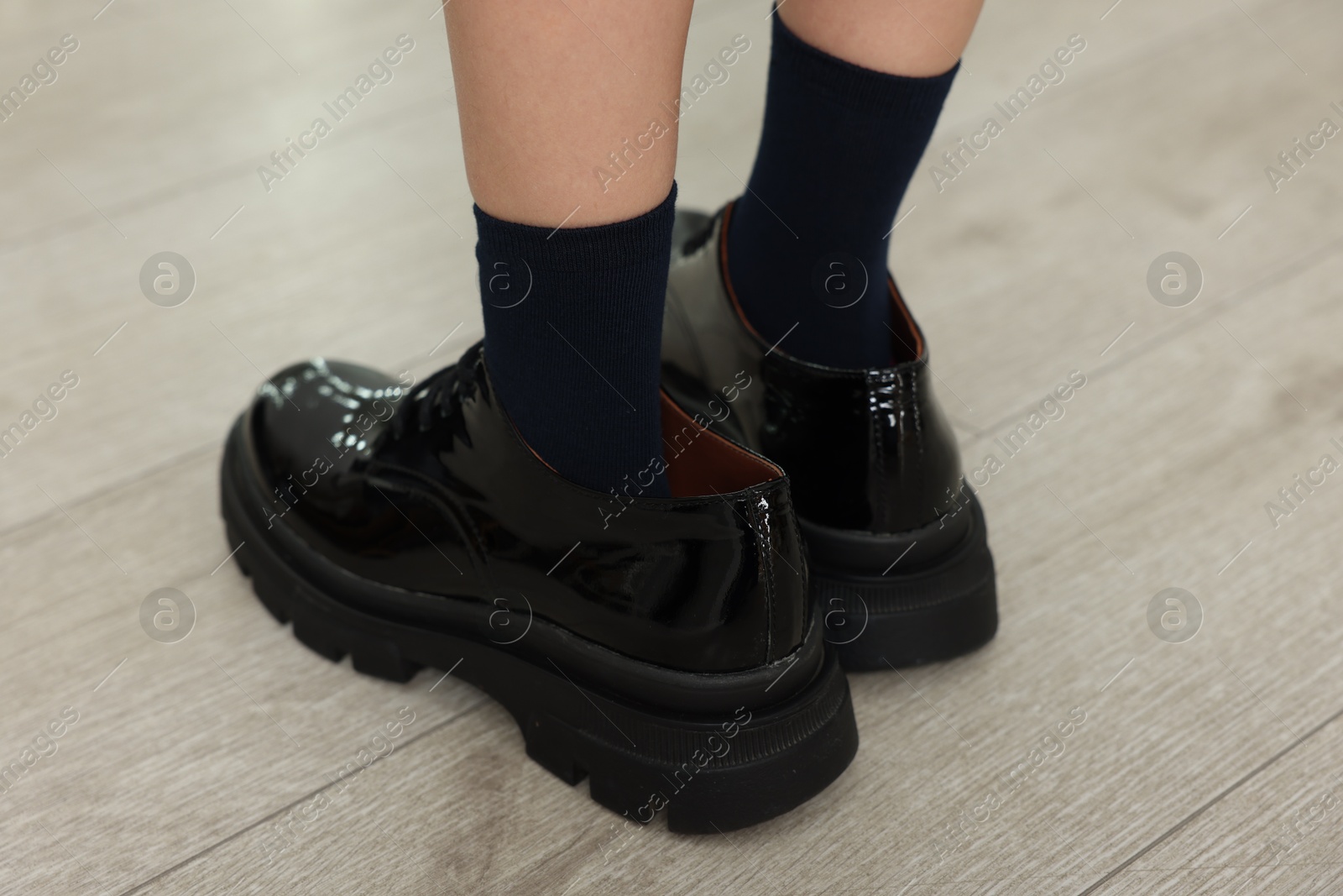 Photo of Little girl wearing oversized shoes indoors, closeup