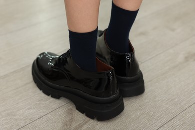 Photo of Little girl wearing oversized shoes indoors, closeup