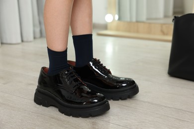 Photo of Little girl wearing oversized shoes indoors, closeup