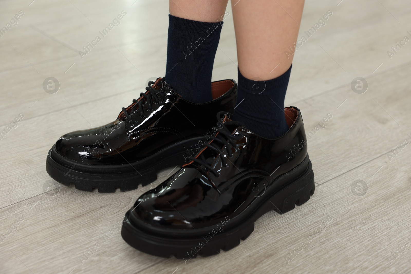 Photo of Little girl wearing oversized shoes indoors, closeup