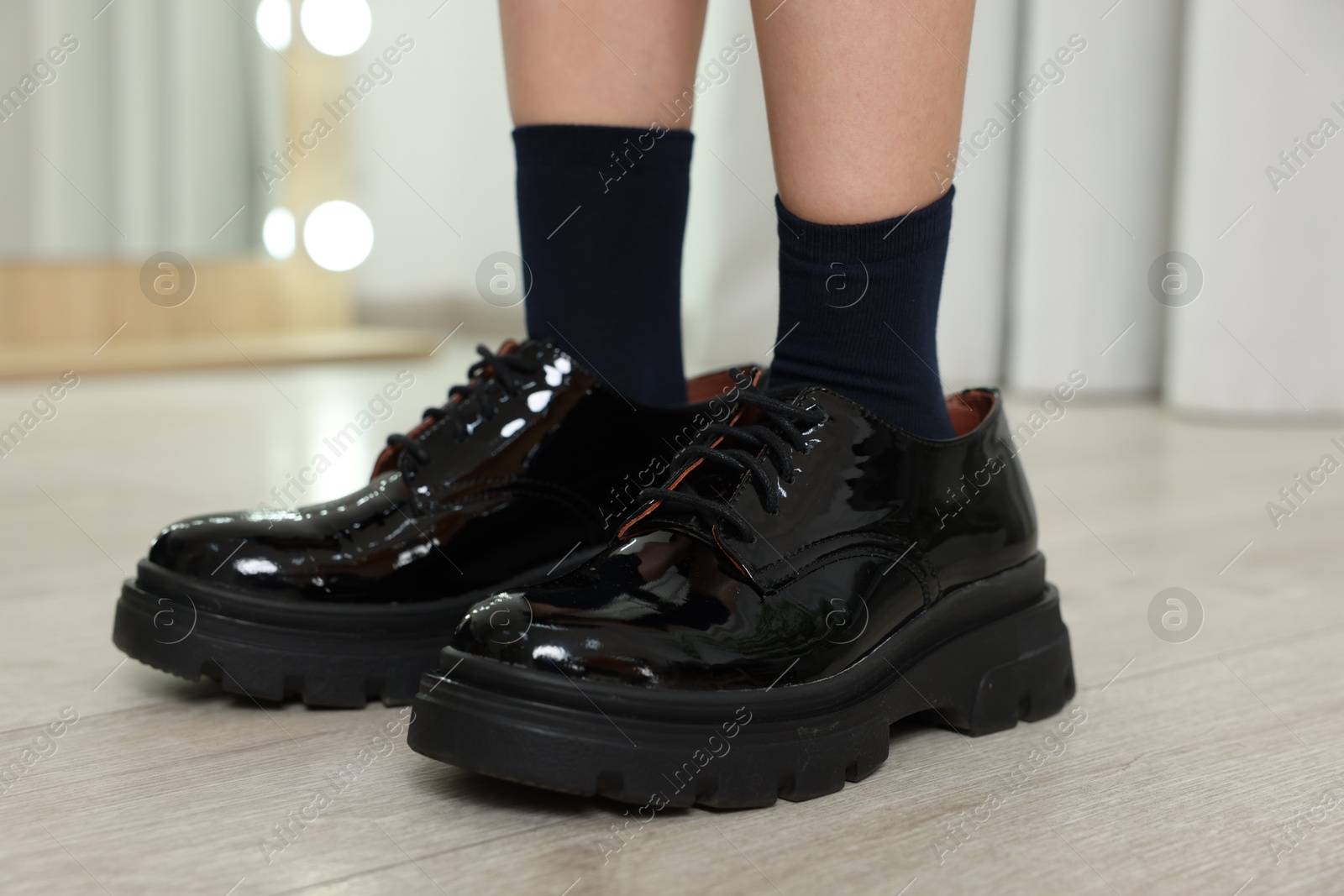 Photo of Little girl wearing oversized shoes indoors, closeup