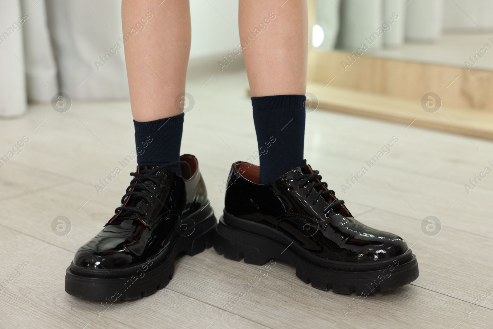 Photo of Little girl wearing oversized shoes indoors, closeup