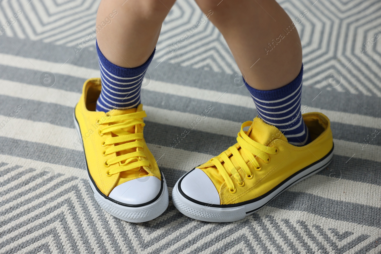 Photo of Child wearing oversized yellow sneakers indoors, closeup