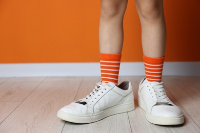 Photo of Child wearing oversized sneakers near orange wall indoors, closeup. Space for text