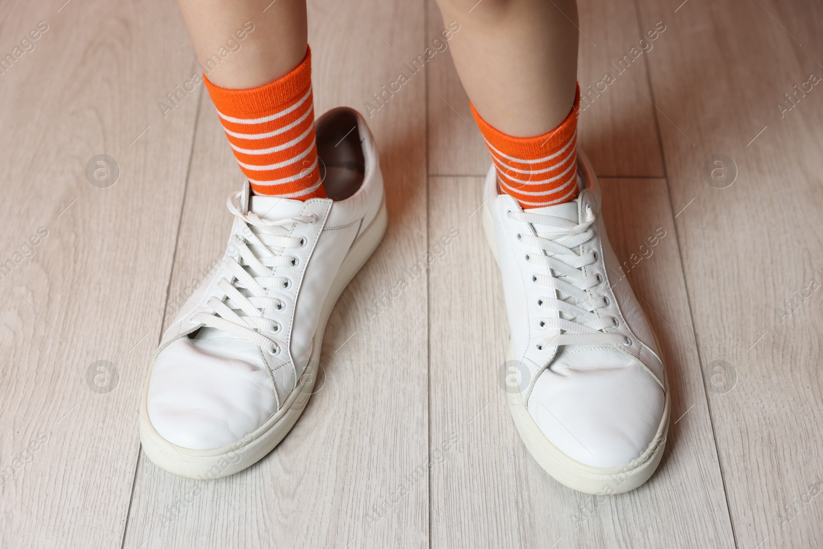 Photo of Little girl wearing oversized sneakers indoors, closeup