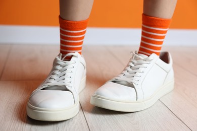 Photo of Child wearing oversized sneakers near orange wall indoors, closeup