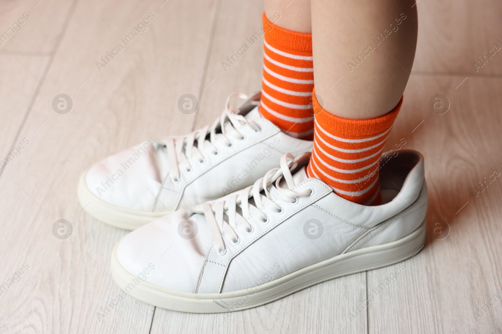 Photo of Little girl wearing oversized sneakers indoors, closeup