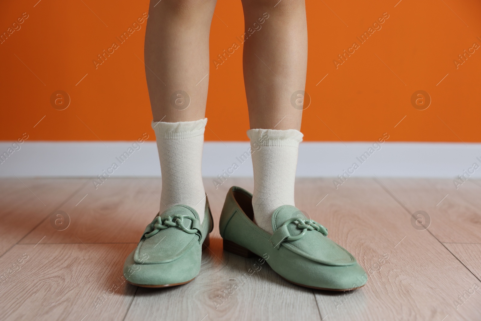 Photo of Child wearing oversized shoes near orange wall indoors, closeup