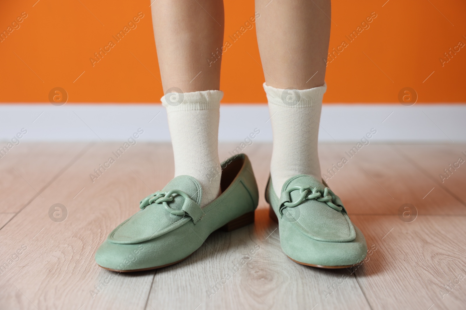 Photo of Child wearing oversized shoes near orange wall indoors, closeup