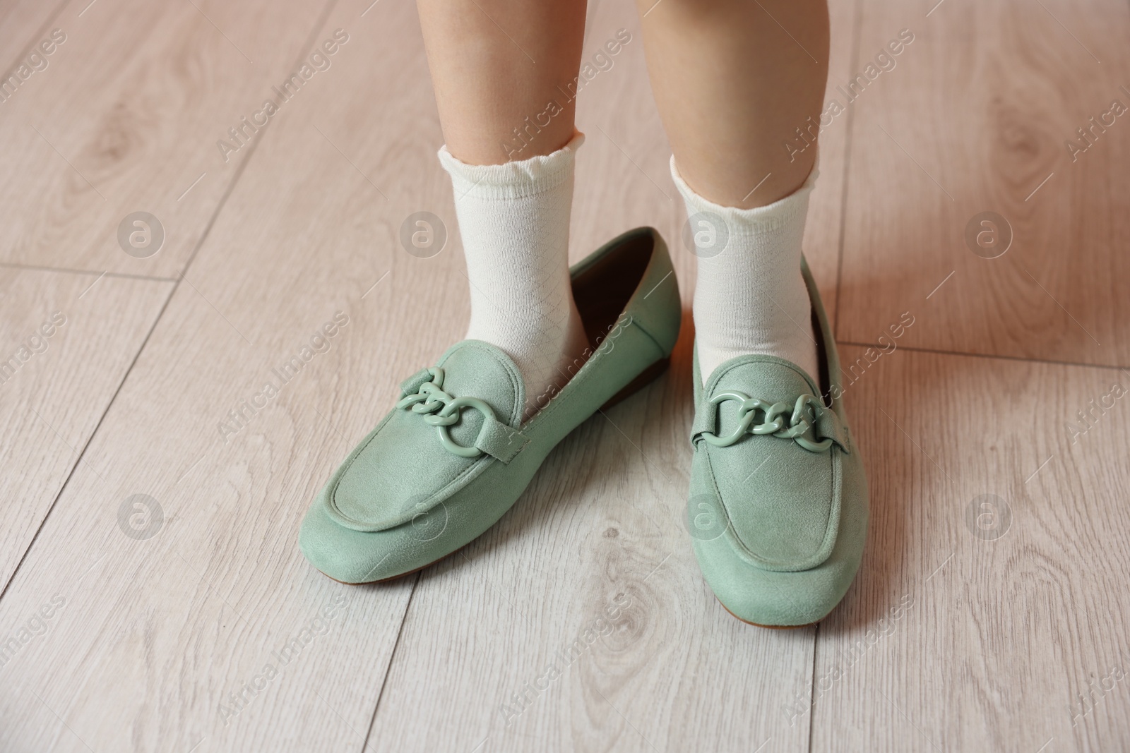 Photo of Little girl wearing oversized shoes indoors, closeup