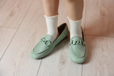 Photo of Little girl wearing oversized shoes indoors, closeup