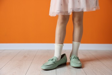 Photo of Child wearing oversized shoes near orange wall indoors, closeup. Space for text