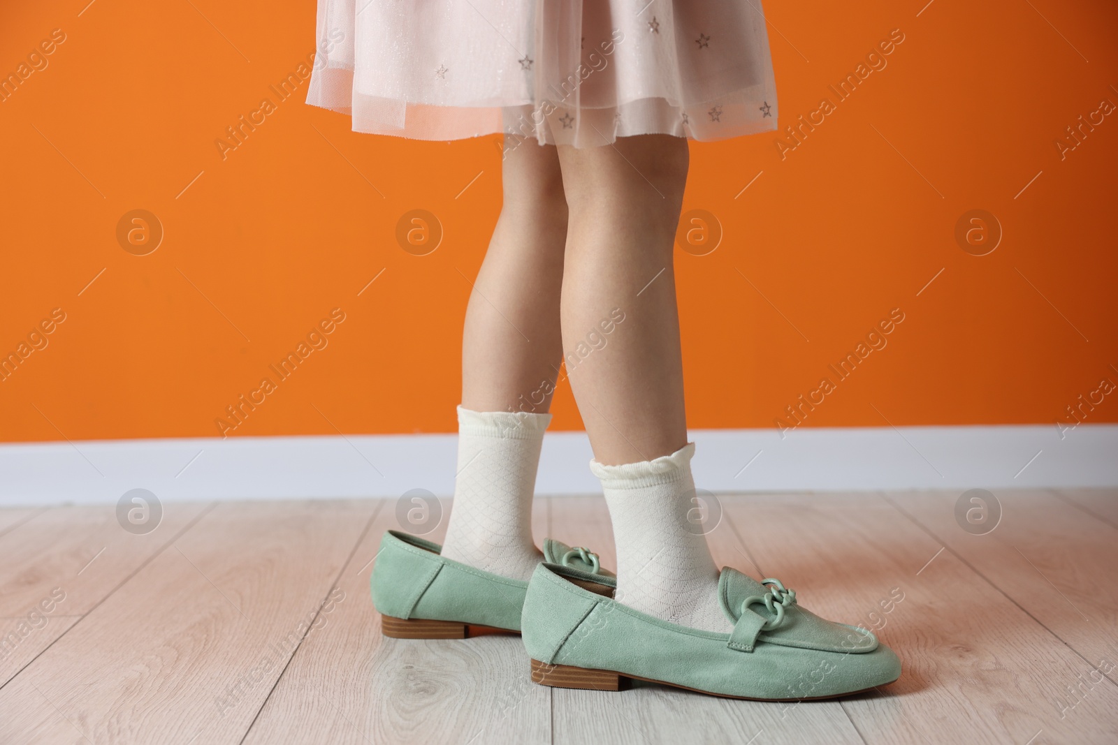 Photo of Child wearing oversized shoes near orange wall indoors, closeup