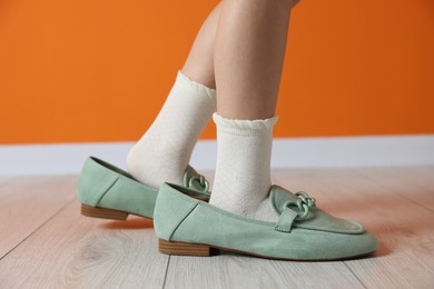 Photo of Child wearing oversized shoes near orange wall indoors, closeup