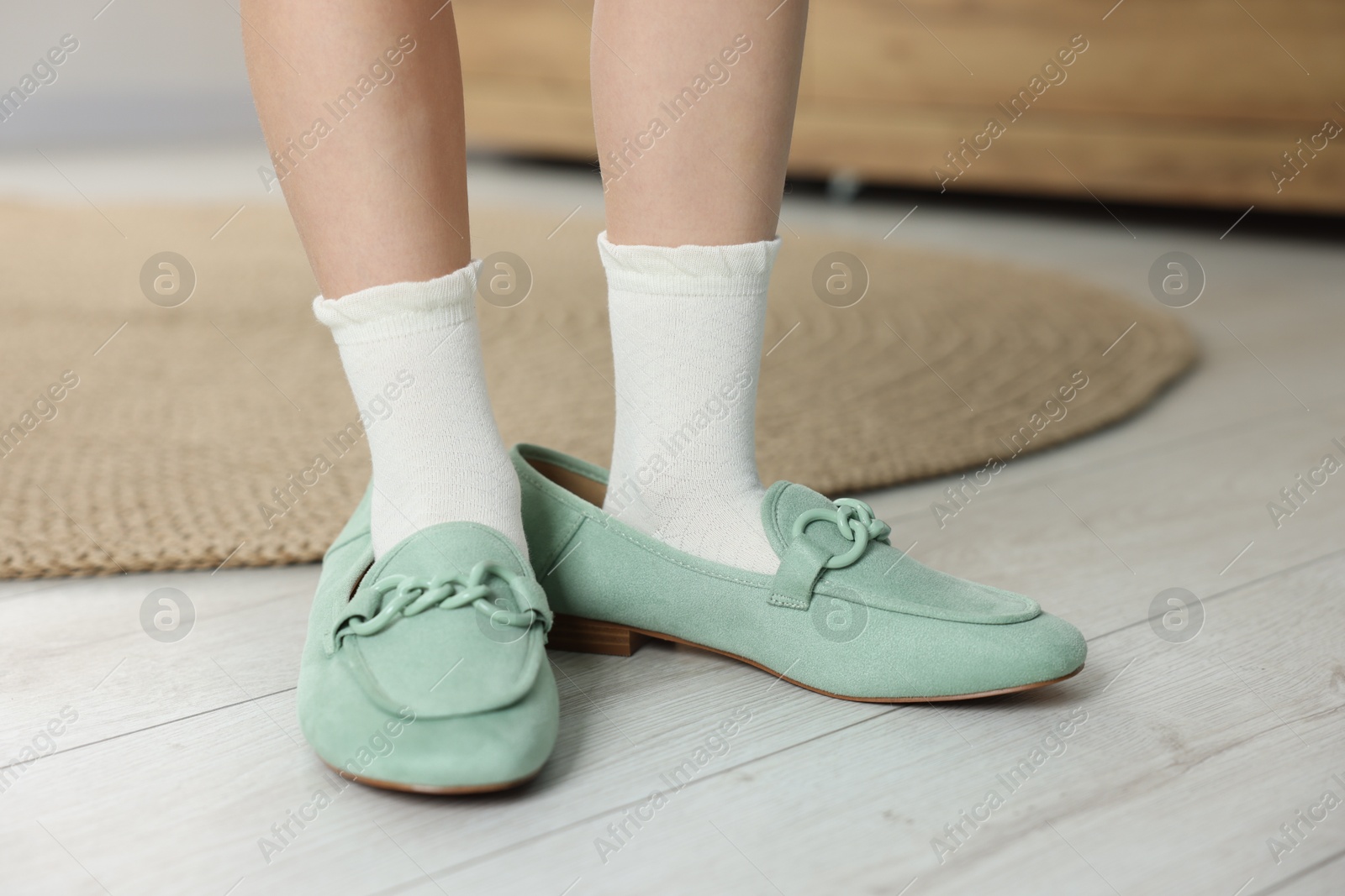 Photo of Little girl wearing oversized shoes indoors, closeup