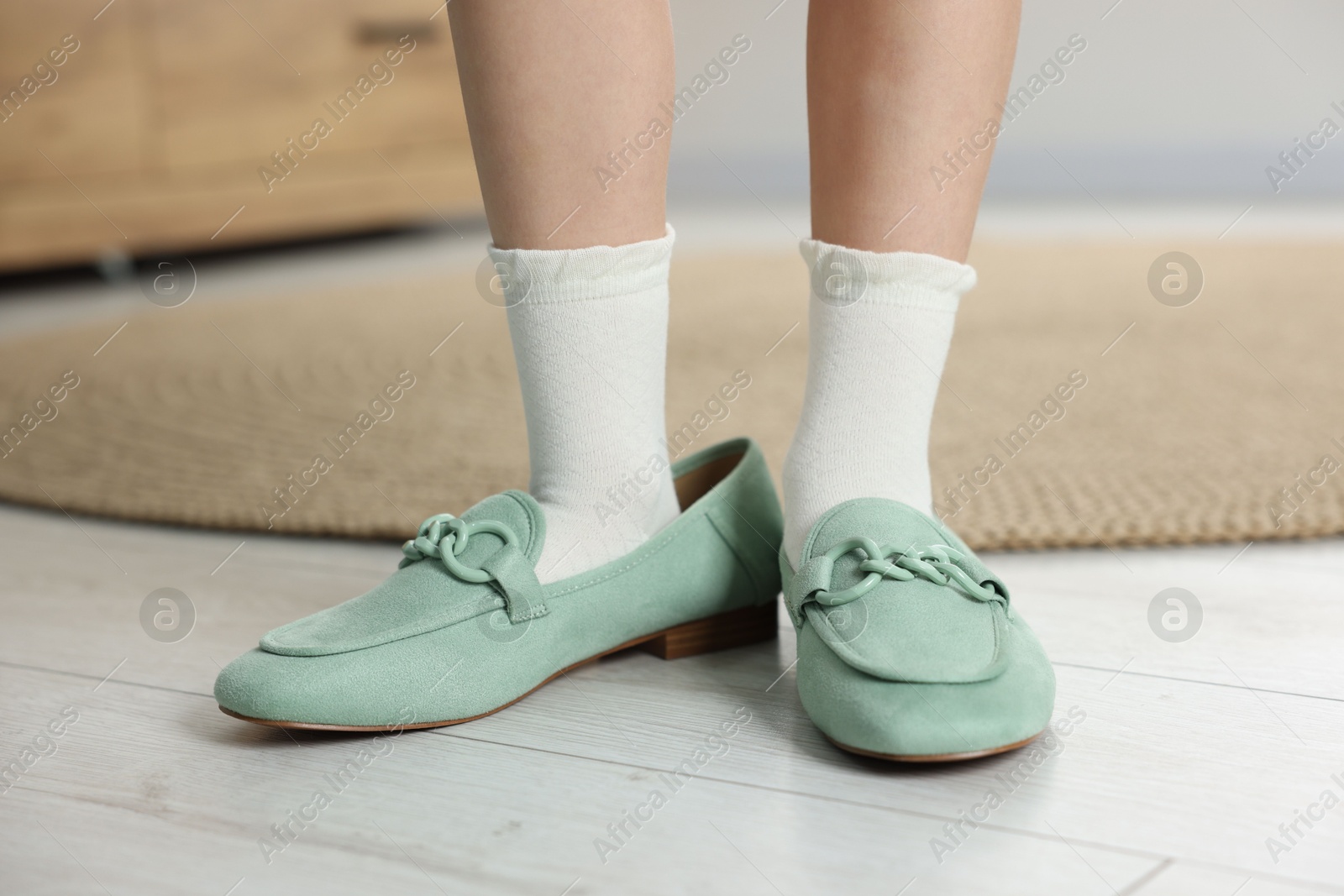 Photo of Little girl wearing oversized shoes indoors, closeup