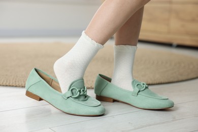 Photo of Little girl wearing oversized shoes indoors, closeup