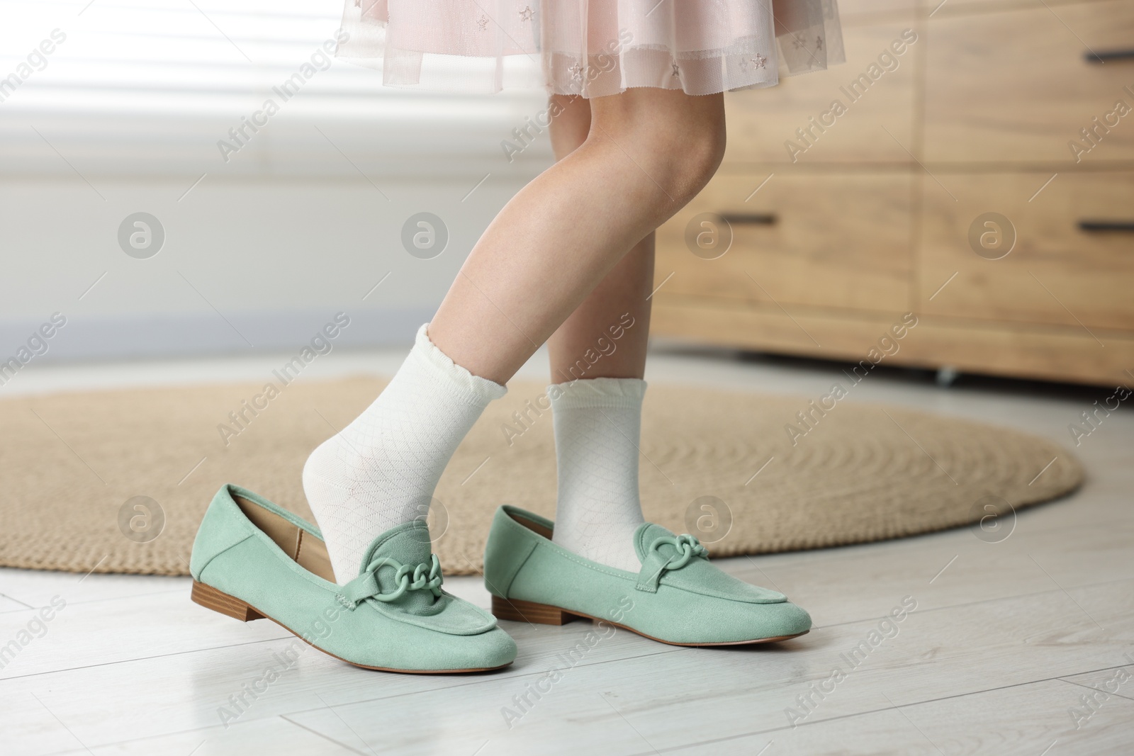 Photo of Little girl wearing oversized shoes indoors, closeup