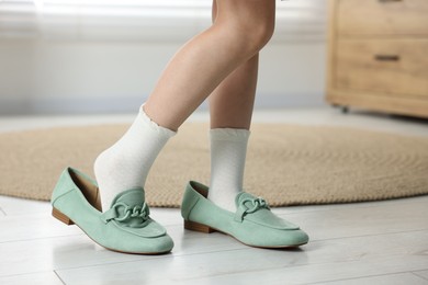 Photo of Little girl wearing oversized shoes indoors, closeup