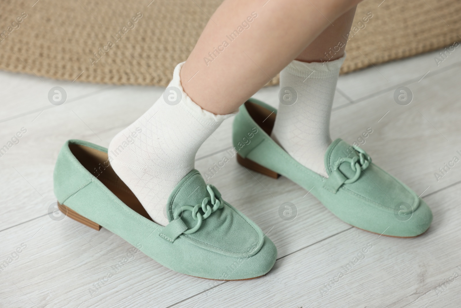 Photo of Little girl wearing oversized shoes indoors, closeup