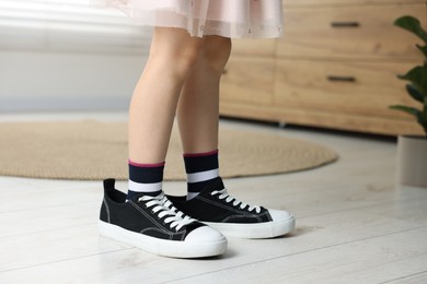 Photo of Child wearing oversized black sneakers indoors, closeup