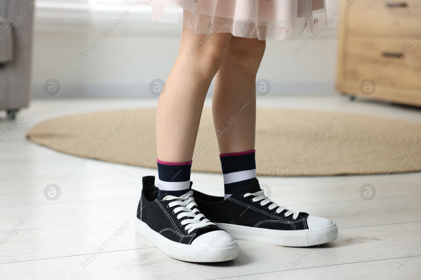 Photo of Child wearing oversized black sneakers indoors, closeup