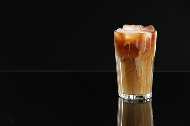 Photo of Refreshing iced coffee with milk in glass on black mirror surface. Space for text