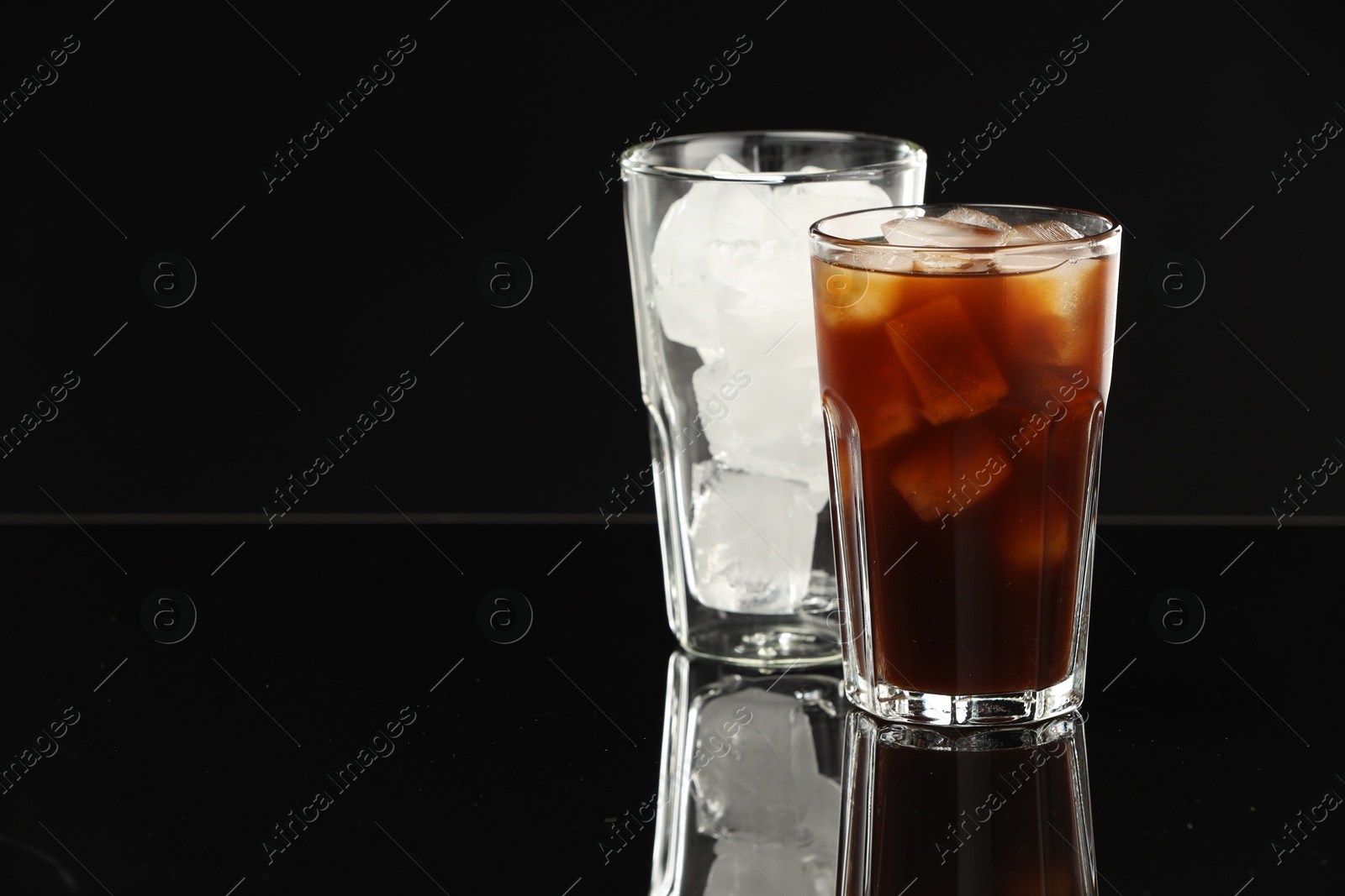 Photo of Refreshing iced coffee and ice cubes in glasses on black mirror surface. Space for text