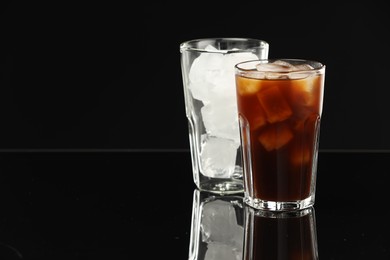 Photo of Refreshing iced coffee and ice cubes in glasses on black mirror surface. Space for text