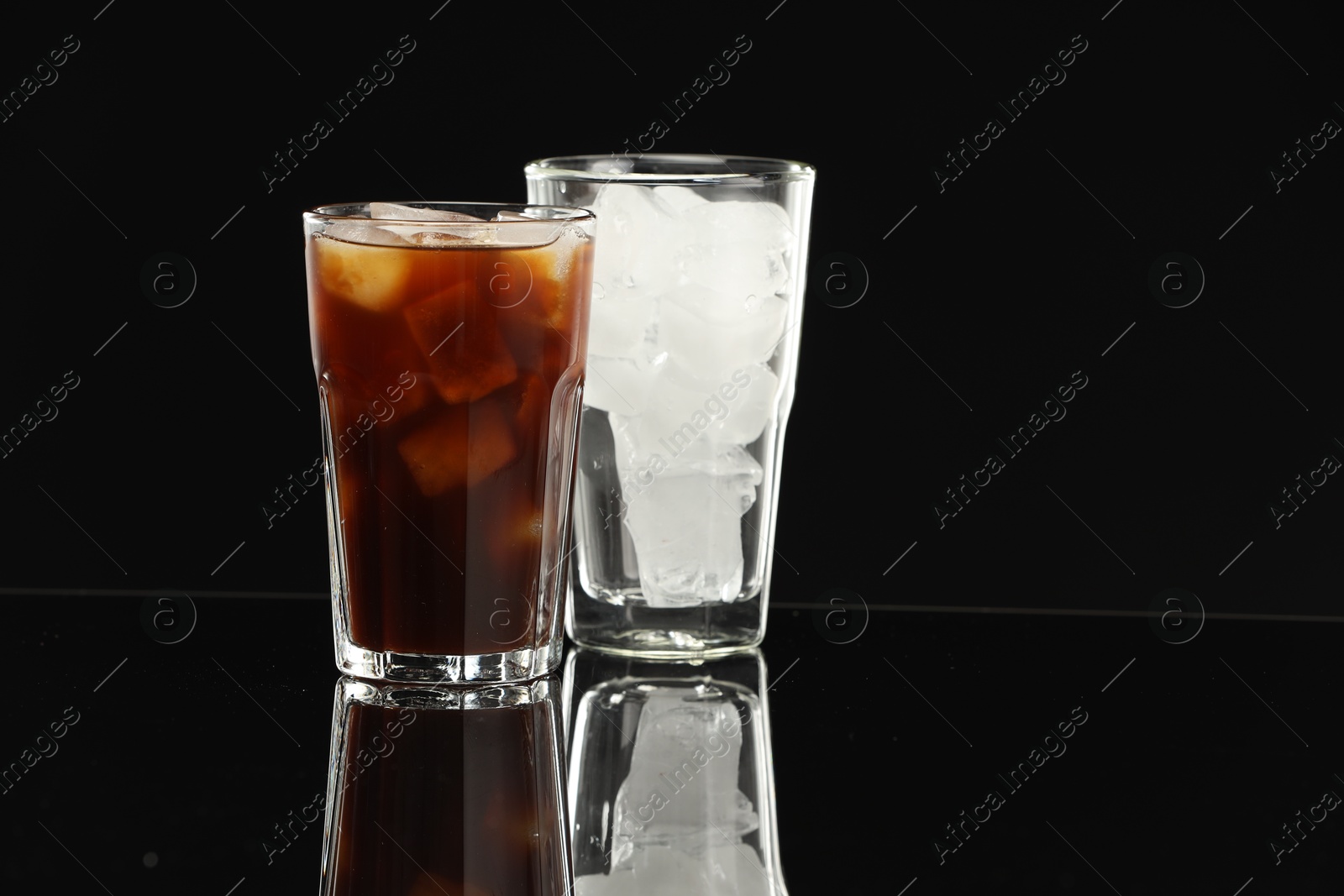 Photo of Refreshing iced coffee and ice cubes in glasses on black mirror surface. Space for text