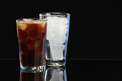 Photo of Refreshing iced coffee and ice cubes in glasses on black mirror surface. Space for text