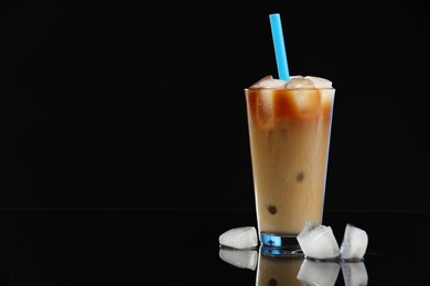 Photo of Refreshing coffee with ice and milk in glass on black mirror surface. Space for text