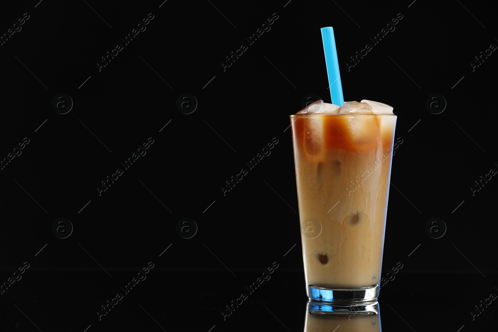 Photo of Refreshing iced coffee with milk in glass on black mirror surface. Space for text