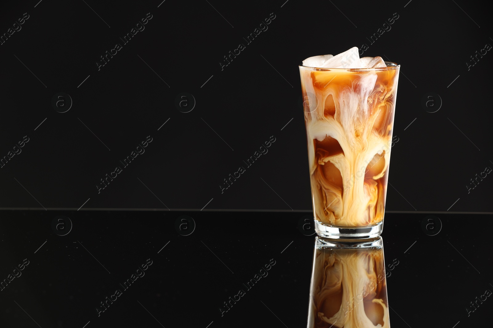 Photo of Refreshing iced coffee with milk in glass on black mirror surface. Space for text