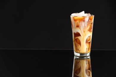 Photo of Refreshing iced coffee with milk in glass on black mirror surface. Space for text