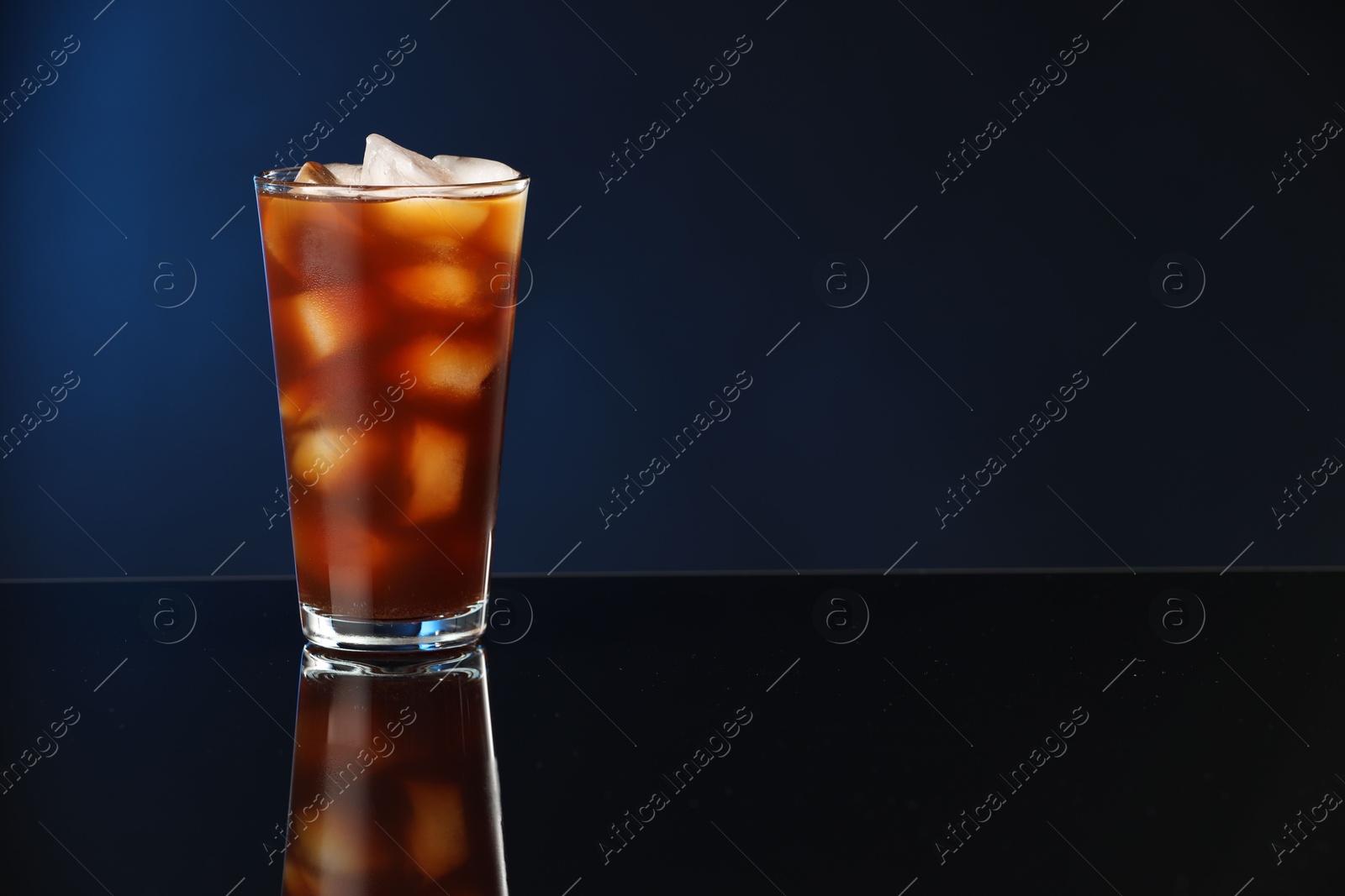 Photo of Refreshing iced coffee in glass on mirror surface. Space for text