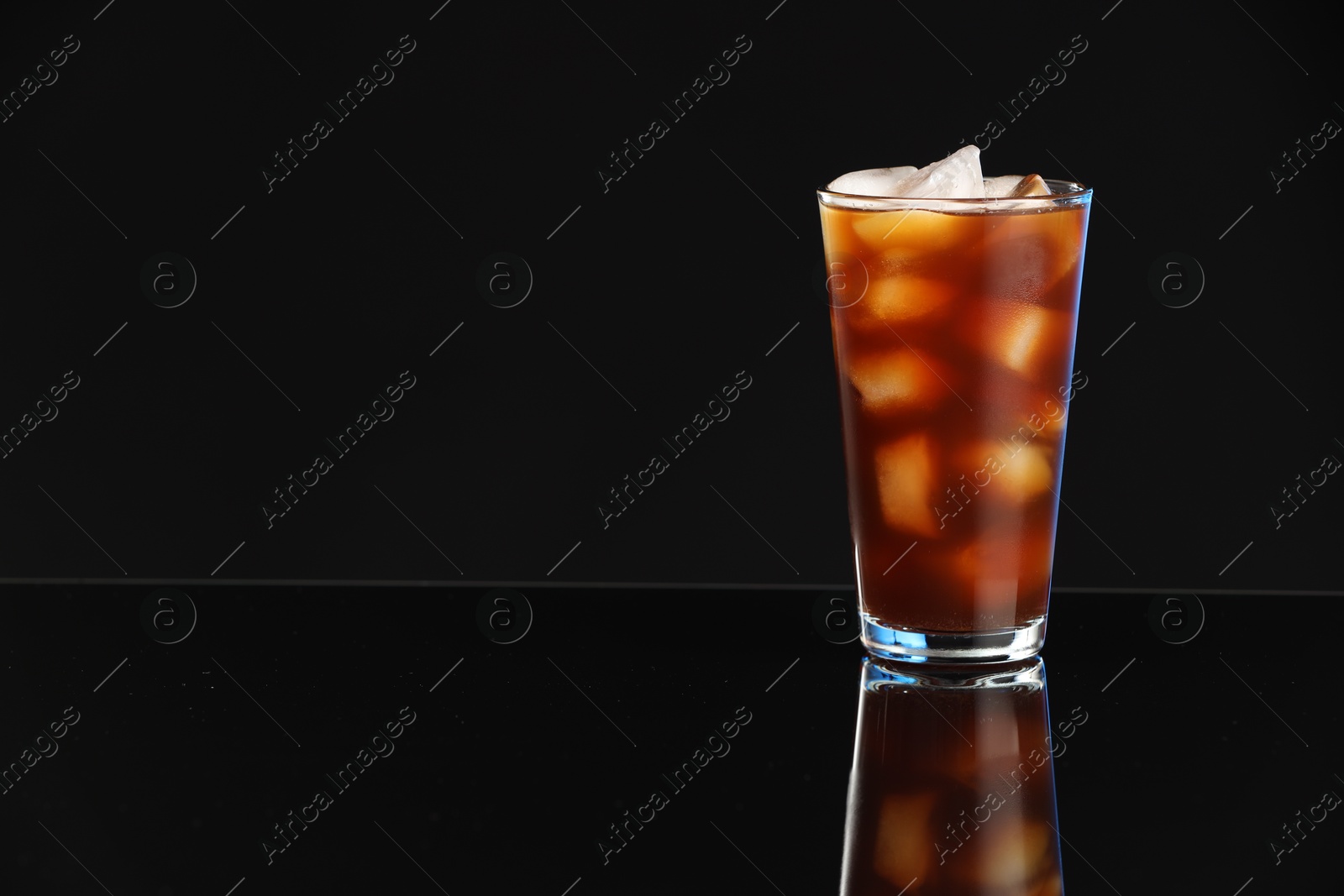 Photo of Refreshing iced coffee in glass on black mirror surface. Space for text