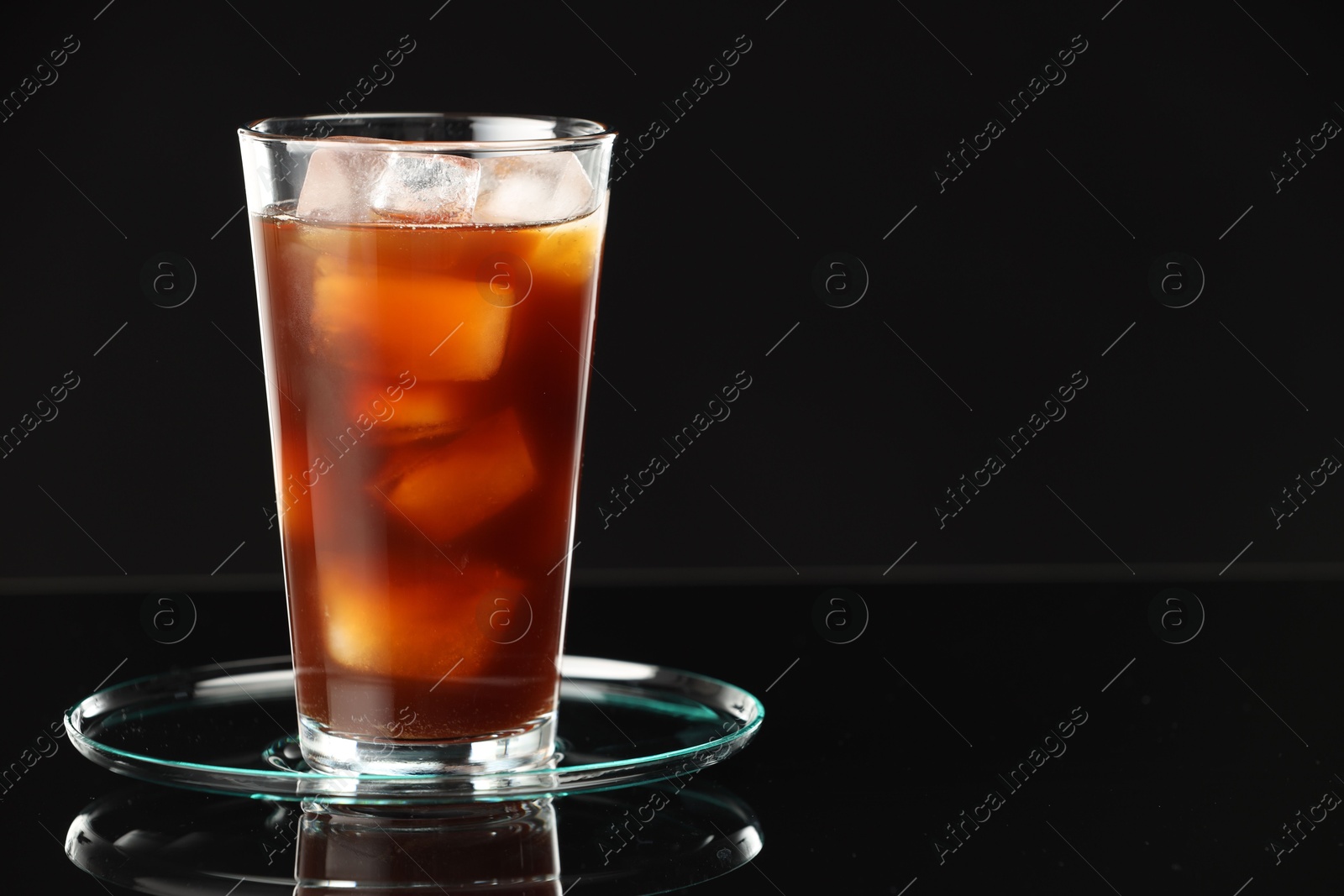 Photo of Refreshing iced coffee in glass on black mirror surface, closeup. Space for text