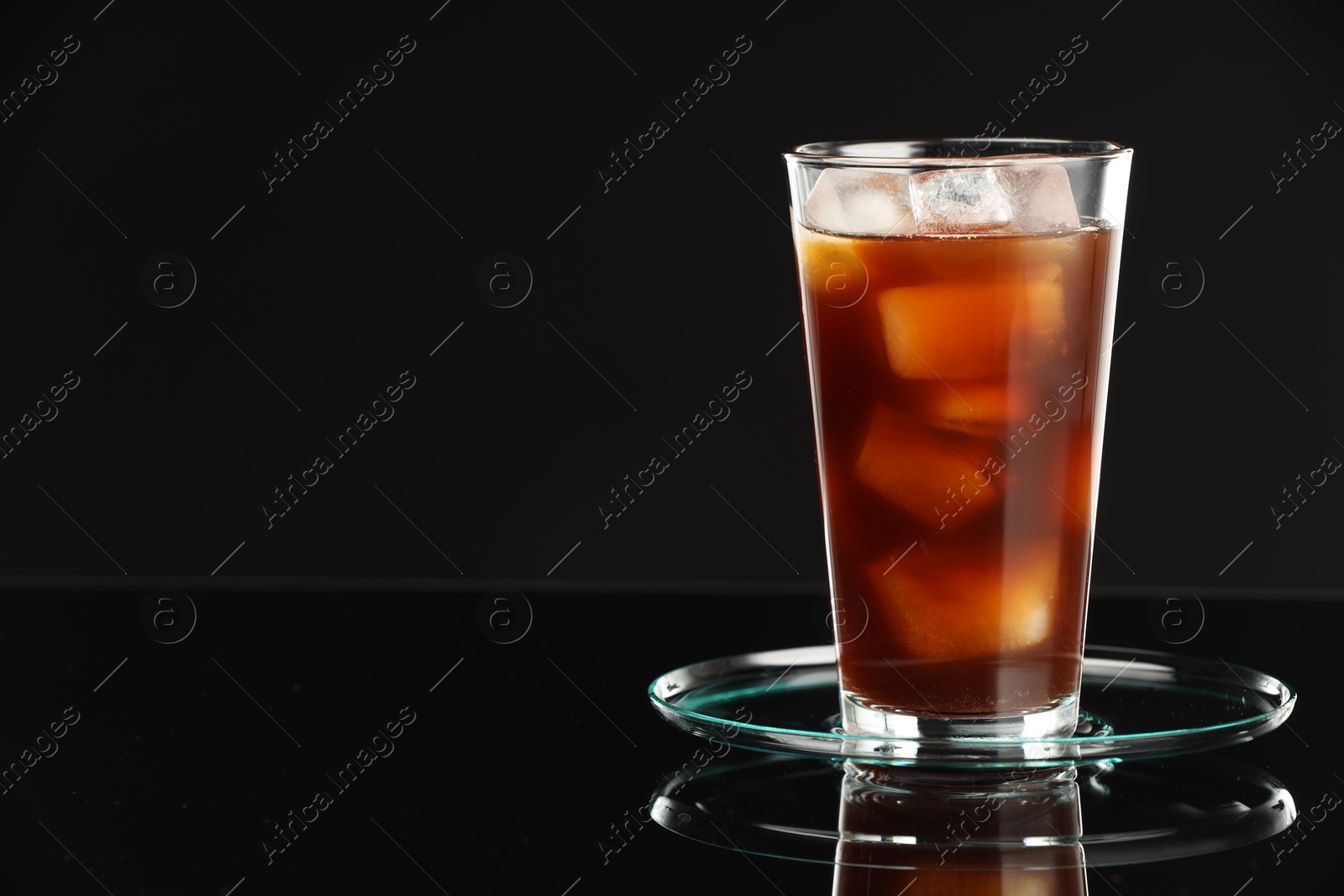 Photo of Refreshing iced coffee in glass on black mirror surface, closeup. Space for text