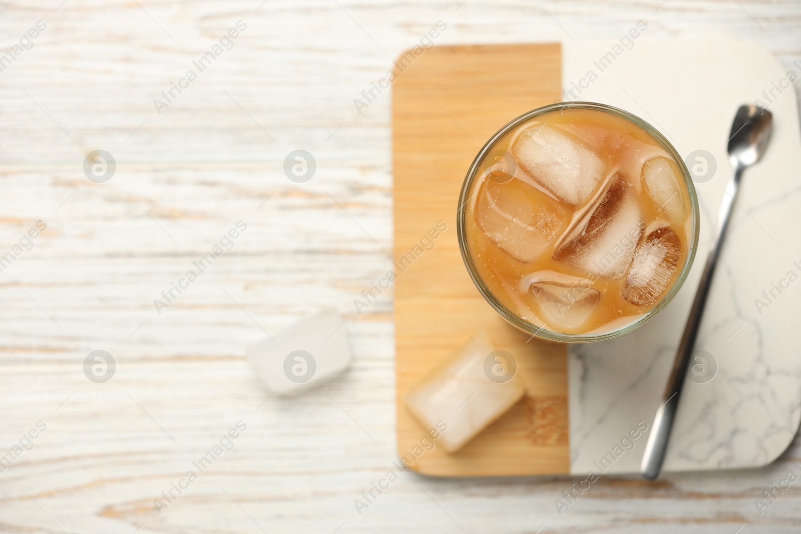 Photo of Refreshing coffee with ice in glass on white wooden table, top view. Space for text