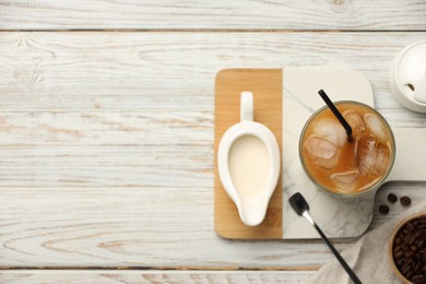 Photo of Refreshing iced coffee in glass, milk and beans on white wooden table, flat lay. Space for text