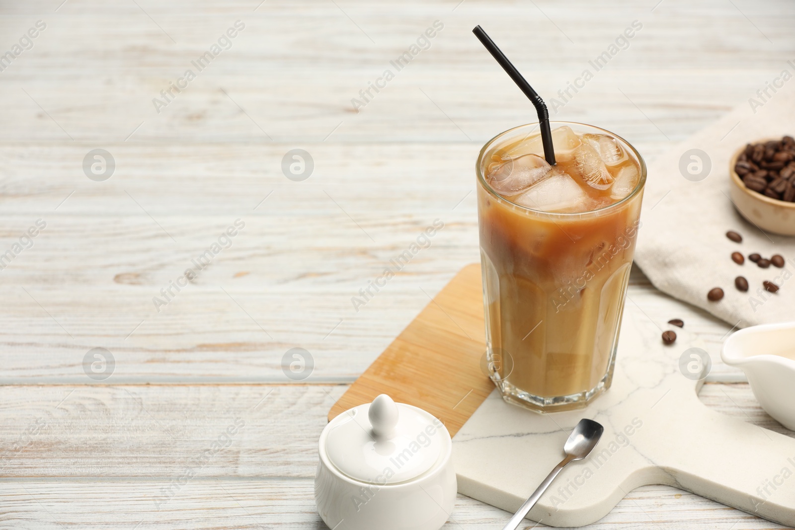 Photo of Refreshing iced coffee with milk in glass and beans on white wooden table. Space for text